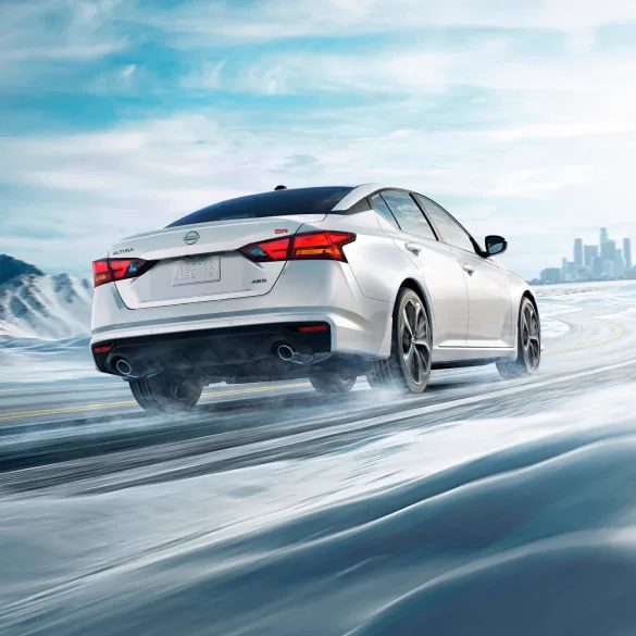 2027 Nissan Altima in white seen from behind driving in snowy landscape illustrating all-wheel drive at Holler Nissan Lexington in Lexington SC